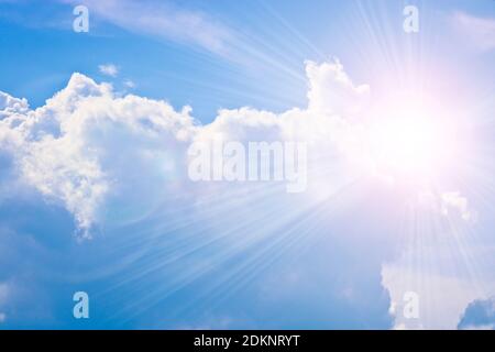 Cumulus and cirrus clouds and bright sunbeams against the blue sky. Atmospheric phenomenon, weather, summer. Stock Photo