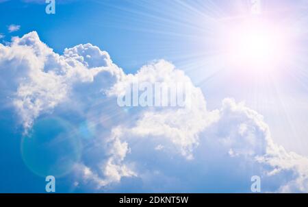 Cumulus and cirrus clouds and bright sunbeams against the blue sky. Atmospheric phenomenon, weather, summer. Stock Photo