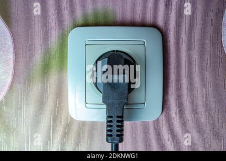 the electric plug is plugged into a wall outlet Stock Photo