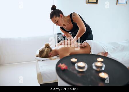 Masseuse doing massage on woman back with aromatherapy oil by her hand Stock Photo