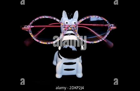 Colorful girl spectacles on a funny zebra shape stand isolated on black background. Children eyewear concept, pink glass frame close up. Stock Photo