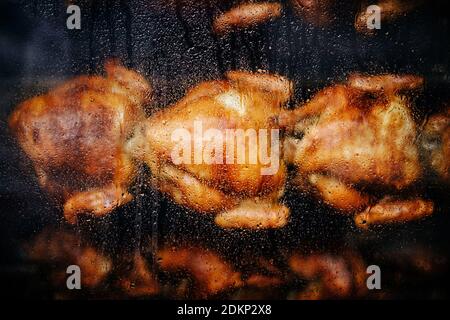 Close-up shot of a steamy rotisserie machine window with water drops. Grilled roasted whole chickens with tasty golden-yellow roasted skin on a spit. Stock Photo
