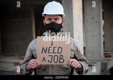 Engineer in mask and hardhat stands with placard I need a job Stock Photo
