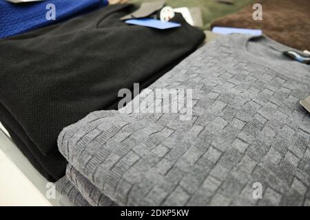 Men knitted sweaters in pastel colors stacked on store counter Stock Photo