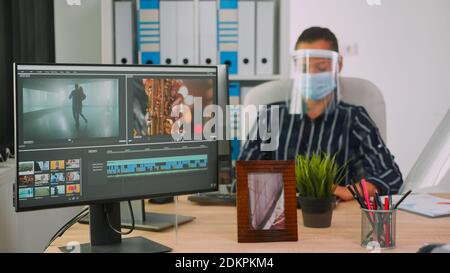Videographers with protection masks working at video project creating content, team of bloggers sitting in new normal office studio. Freelancers editing video durig global pandemic Stock Photo