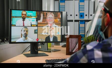 Back view of business man in wheelchair talking to colleagues about plan in video conference wearing visor in new normal office. Immobilized freelancer working in company respecting social distance Stock Photo