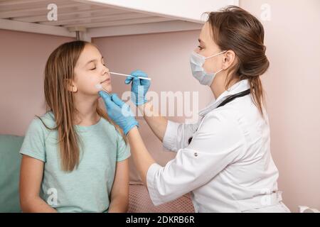 Pediatrician taking nasal mucus test sample from elementary age girl's nose performing respiratory virus testing procedure at home during coronavirus Stock Photo