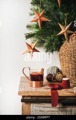 Cup of mulled wine over wooden kitchen counter with Christmas festive decorative baubles and stars and Christmas tree branches at background. Winter holiday mood concept Stock Photo