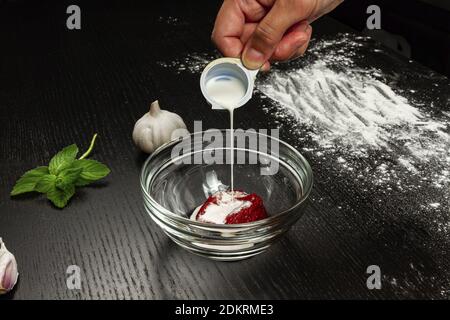 girl chef pours cream into tomato paste for making fresh italian homemade pizza Stock Photo