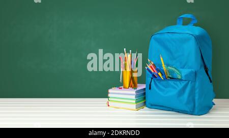 School bag with supplies for school on blackboard background. Copy space for text. Stock Photo