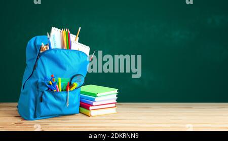 School bag. Backpack with supplies for school on the background of green blackboard. Copy space for text Stock Photo