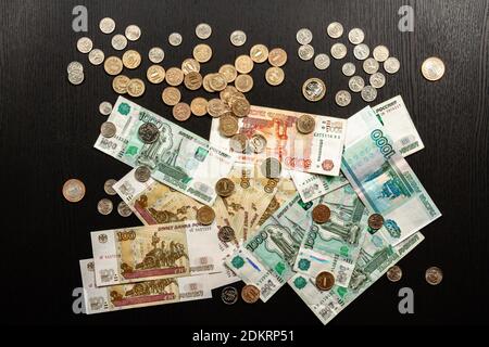 a lot of Russian metal coins and paper money lie on a black wooden table Stock Photo