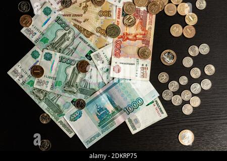 a lot of Russian metal coins and paper money lie on a black wooden table Stock Photo