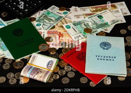 employment history and military ID and coins with banknotes lie on a black wooden table inscription employment history russian federation Stock Photo