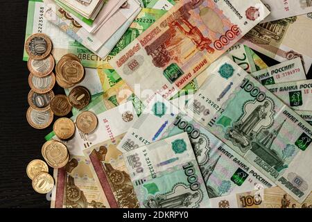 a lot of Russian metal coins and paper money lie on a black wooden table Stock Photo