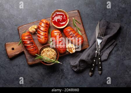 Hot grilled sausages on wooden board with ketchup and mustard. Top view flat lay Stock Photo