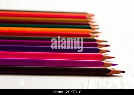 many colored sharpened pencils lie on a white wooden table Stock Photo