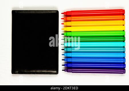black leather wallet and bright colored markers without caps lie on a white wooden table Stock Photo