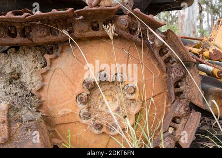 A close up of mud filled and rusted caterpillar tracks on an old bulldozer sitting in long grass in a junk yard in Australia Stock Photo