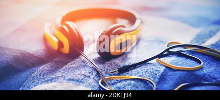 Large yellow headphones with a long wire lie on a soft blue plaid wool blanket, illuminated by bright sunlight. Inspiration and hobbies. Listen to ple Stock Photo