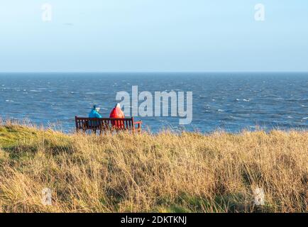 Two people sitting on a bench looking out to sea Stock Photo
