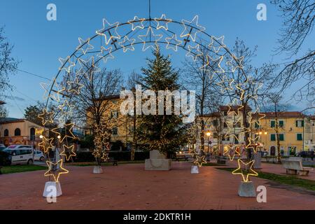 Star-shaped fairy lights arches and decorated Christmas tree in Piazza Vittorio Emanuele II in Bientina, Pisa, Italy, at dusk Stock Photo