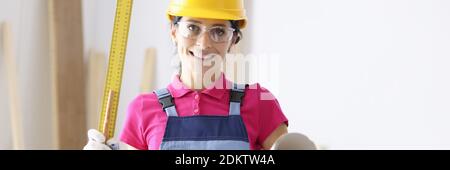 Woman builder in protective helmet and goggles holding wallpaper and ruler Stock Photo