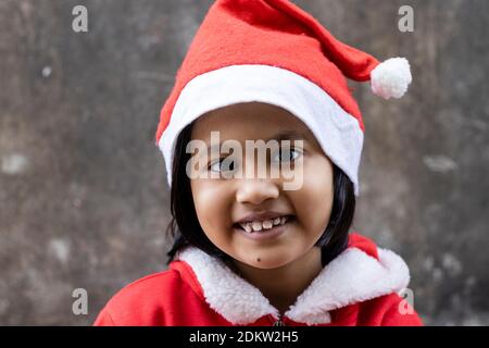 portrait of an Indian girl child smiling in santa claus dress and hat Stock Photo