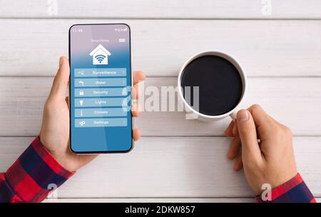 Man Controlling Smart Home Processes With App On Smartphone And Drinking Coffee Stock Photo