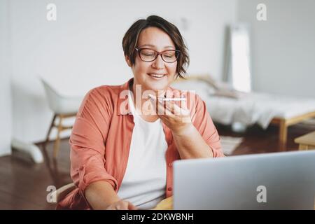 Adult charming brunette woman in glasses plus size body positive working with laptop at home Stock Photo