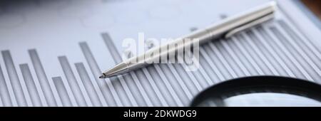 Ballpoint pen and magnifying glass lying on documents with graph in office closeup Stock Photo