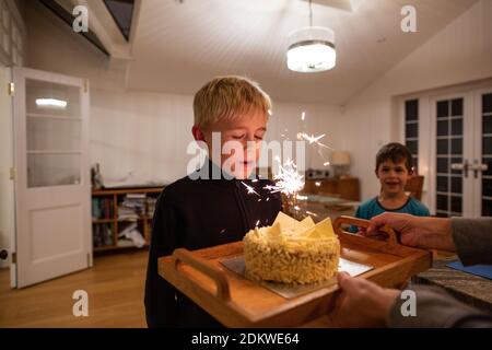 10-year-old boy blows out the candle on his birthday cake whilst his younger brother watches, England, United Kingdom Stock Photo