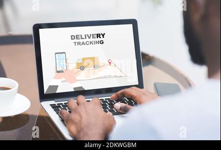 Black Man Using Delivery Tracking Service On Laptop While Sitting In Cafe Stock Photo