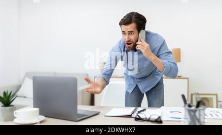 Angry Businessman Talking On Phone Standing In Office Stock Photo