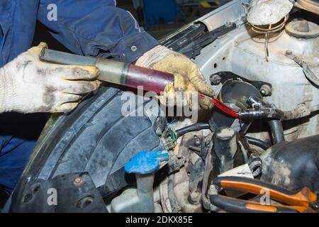 The mechanic's gloved hands hold a syringe of red oil. Replacing the fluid in the car's power steering system Stock Photo