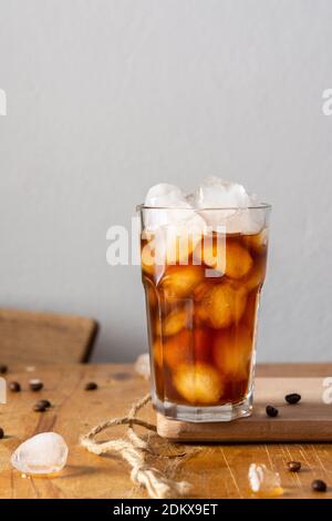Cold refreshing iced coffee in a glass on a wooden board close-up, cocoa beans are scattered on the table Stock Photo