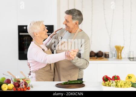 Cheerful Elderly Couple Dancing In Kitchen Having Fun At Home Stock Photo