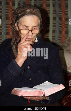 Elderly woman in Romania's countryside reading from the Bible Stock Photo