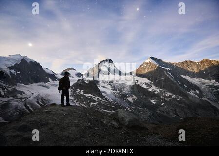 Unbelievably beautiful starry night illuminated by the Moon in Switzerland Alps, man standing and enjoying this peaceful scene of silent snowy peak Dent Blanche Stock Photo