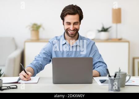 Business Guy Working Taking Notes Sitting At Laptop In Office Stock Photo