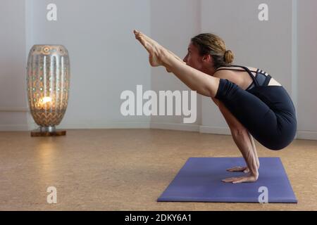 Strong woman in tittibhasana standing on hands with legs upwards at yoga studio. Flexible female yogi practicing ashtanga firefly pose. Core strength Stock Photo
