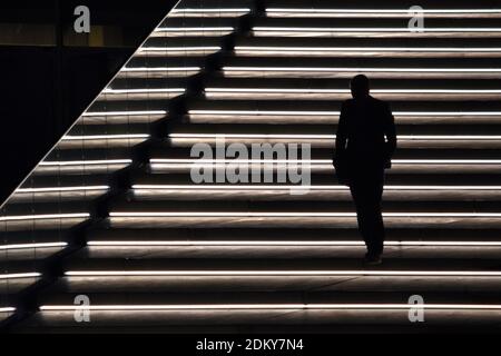Silhouette of man walking down on illuminated staircase at night Stock Photo