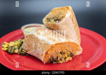 Veggie burrito loaded with fresh vegetables cut in half and presented on a red plate. Stock Photo