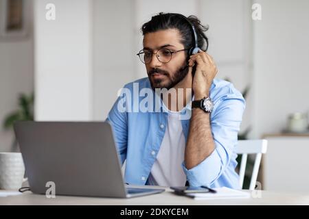 Focused Arab Guy In Headset Watching Webinar On Laptop At Home Stock Photo