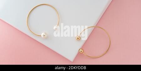Two golden with pearls bracelets on pink and white background Stock Photo