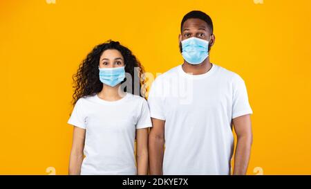 Multiethnic Couple Wearing Face Masks Posing Over Yellow Studio Background Stock Photo