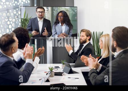 Team of five diverse business people, start up developers, clapping hands while attending videoconference with their multiethnic colleagues or Stock Photo
