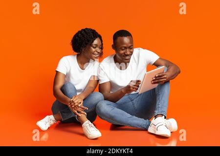 Cheerful black couple using digital tablet over orange Stock Photo