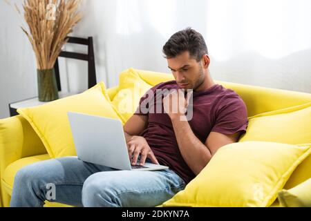 Pensive freelancer using laptop on sofa at home Stock Photo