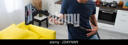 Cropped view of man having fun with brush of vacuum cleaner at home, banner Stock Photo
